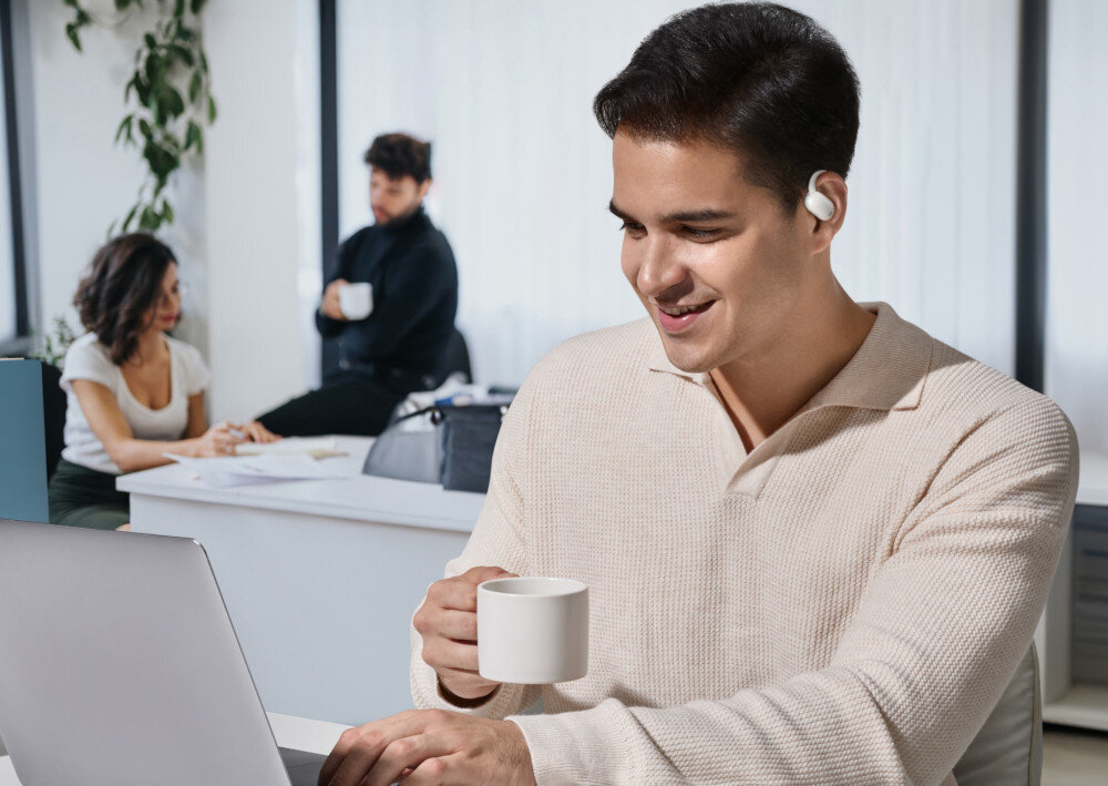 Słuchawki powietrzne SOUNDCORE AeroFit 2 otwarta konstrukcja zaczepy wentylacja higiena, osoba siedząca przy laptopie z założonymi słuchawkami