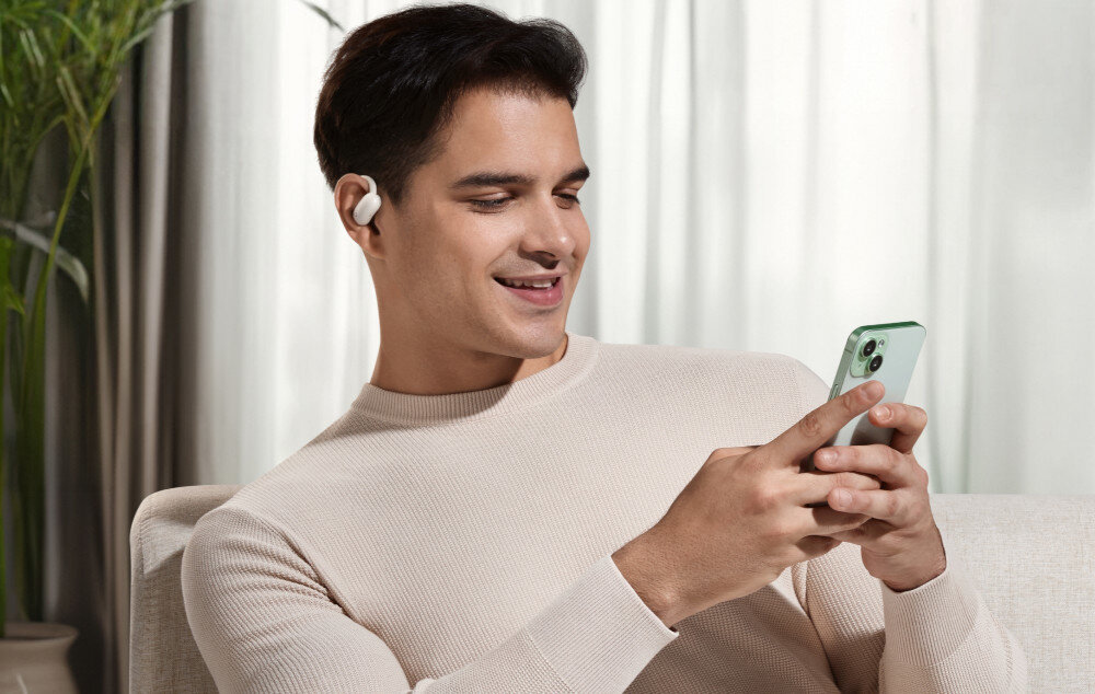 Słuchawki powietrzne SOUNDCORE AeroFit 2 Bluetooth 5.4 multi-point stabilne połączenie, osoba trzymająca telefon w rękach z założonymi słuchawkami