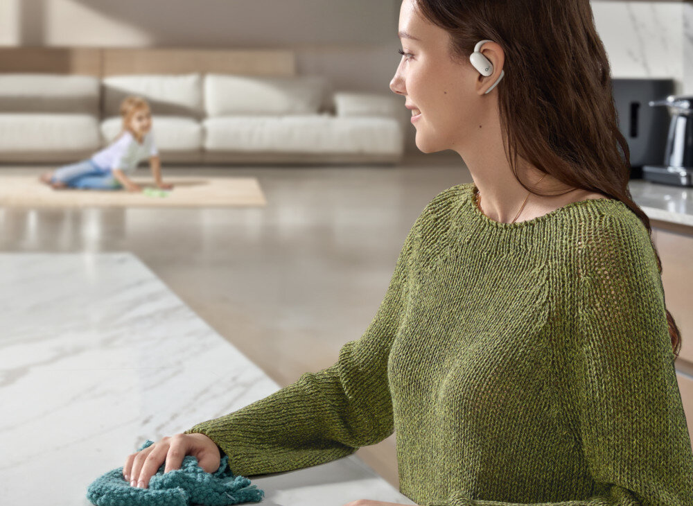 Słuchawki powietrzne SOUNDCORE AeroFit 2 sterowanie dotykowe asystent głosowy wygoda obsługi, osoba stojąca przy blacie z założonymi słuchawkami