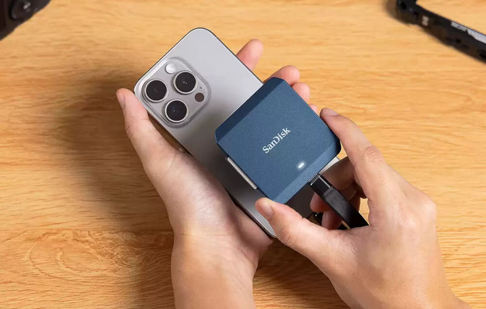 Czytnik kart SANDISK PRO-CINEMA CFexpress Typ B prezentacja czytnika z telefonem iPhone w tle biurko kompatybilność z iPhone 15 Pro i Pro Max przez MagSafe kompatybilność wygoda