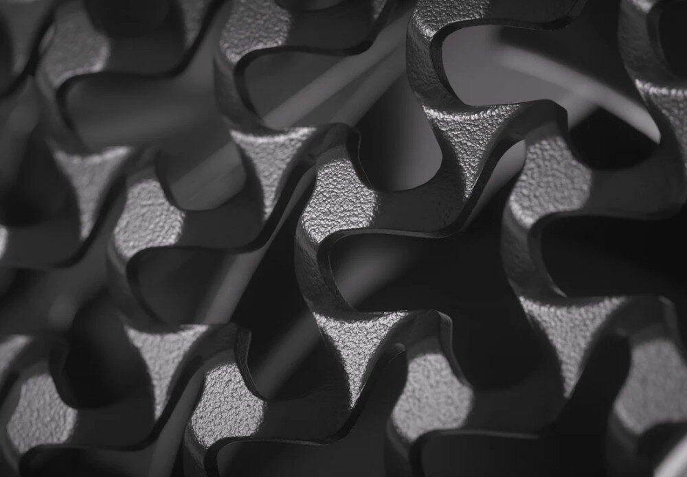 Zbliżenie na teksturę metalowej powierzchni z wyciętymi, falistymi wzorami. Materiał ma ciemny, matowy kolor z widocznymi refleksami światła.