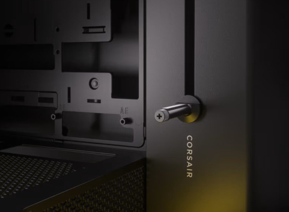 Czarna obudowa komputerowa z widocznym logo \'CORSAIR\' oraz metalowym uchwytem z krzyżowym wkrętem. W tle widać wnętrze obudowy z otworami montażowymi.