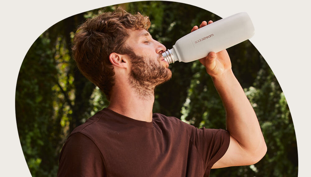 BUTELKA TERMICZNA SODASTREAM DO GAZOWANIA WODY PIASKOWA 0.9L mężczyzna pije napój z beżowej butelki trwałość funkcjonalność styl ulubiony napój hermetyczna konstrukcja silikonowa uszczelka bezpieczeństwo materiały wolne od BPA solidna stal nierdzewna 18/8 odporność na korozję i intensywne użytkowanie proste czyszczenie możliwość mycia w zmywarce