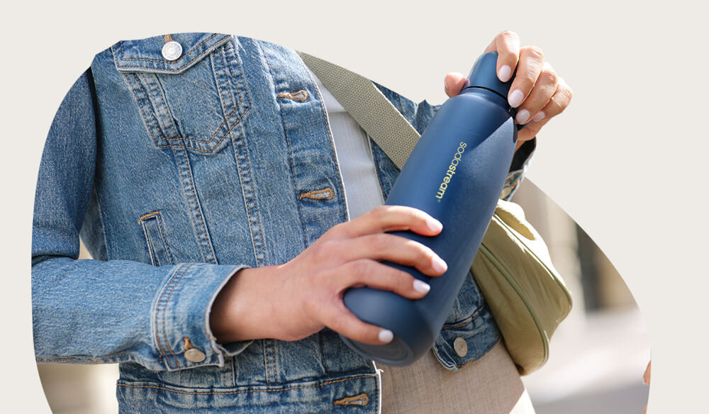 BUTELKA TERMICZNA SODASTREAM DO GAZOWANIA WODY STORM BLUE 0.9L osoba trzyma w ręku butelkę w kolorze granatowym zakrętka uchwyt pojemność 0,9 l funkcjonalność bidonu kubka termicznego butelki do saturatora gazowanie wody bezpośrednio w środku podwójne ścianki do 12 godzin elegancja granatowy elegancki uniwersalny kolor wyrafinowany design funkcjonalność