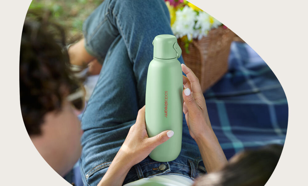BUTELKA TERMICZNA SODASTREAM DO GAZOWANIA WODY MIĘTA 0.9L piknik osoba trzyma w ręku miętową butelkę uchwyt zakrętka pojemność 0,9 l pastelowa mięta 3 w 1 funkcjonalność bidonu kubka termicznego butelka do saturatora świeży design pastelowa mięta w dobrym stylu