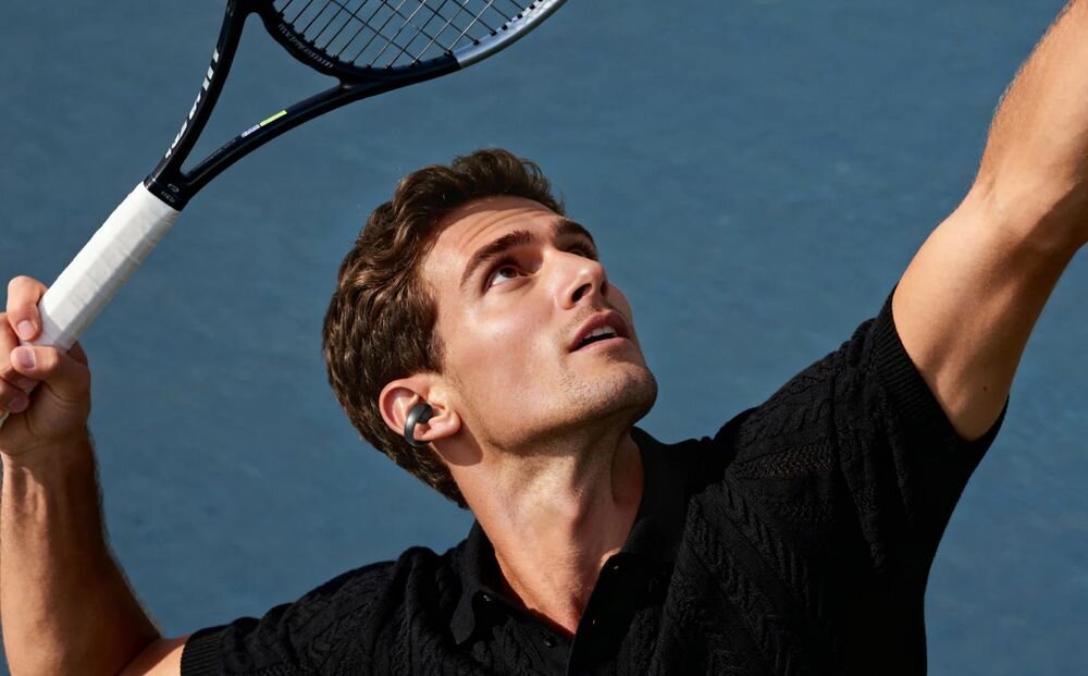 SOUNDCORE AeroClip Open-Ear Clip stabilne dopasowanie sport aktywność wygoda użytkowania, osoba z założonymi słuchawkami powietrznymi grająca w tenisa