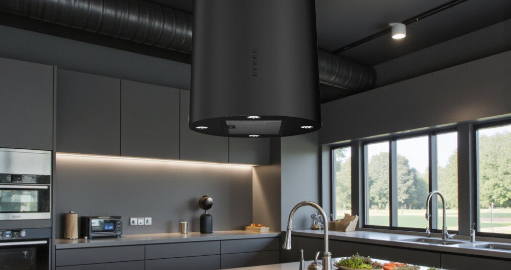 OKAP AKPO WK-12 ISLA BALMERA SLIM Na zdjęciu widać przestronną kuchnię w ciemnej kolorystyce z dużym, czarnym okapem wyspowym zawieszonym nad wyspą kuchenną. W tle znajdują się długie blaty robocze, zabudowa z piekarnikiem, duże okna z widokiem na zieleń oraz dwa zlewy z wysokimi bateriami smukły design minimalistyczny elegancja styl industrialny proporcje