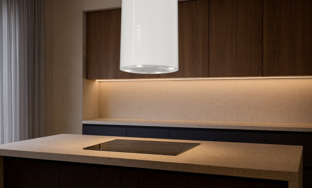 OKAP AKPO WK-4 Isla Balmera Slim Na zdjęciu widać kuchnię z czarnym, cylindrycznym okapem sufitowym zawieszonym nad blatem. W tle znajdują się jasne szafki, zlew z czarną baterią oraz dekoracje w postaci wazonu z gałązkami i butelek.