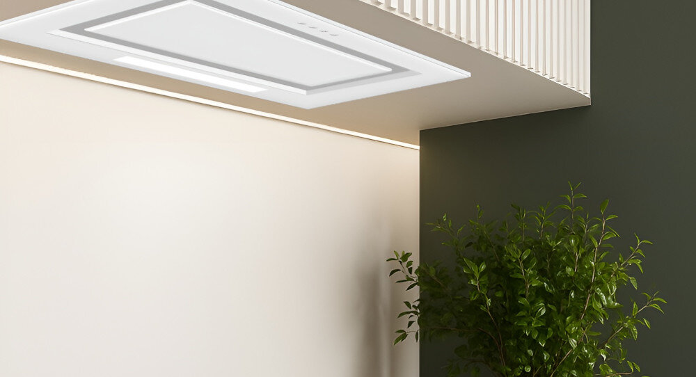 OKAP AKPO WK-11 FABIO 60 Widzimy biały okap sufitowy wbudowany w podwieszany sufit nad jasną strefą kuchenną. Obok znajduje się zielona ściana z rozłożystą rośliną doniczkową, co dodaje wnętrzu świeżości.