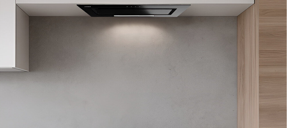 OKAP AKPO WK-11 FABIO 60 Widzimy czarny okap sufitowy wbudowany w podwieszany sufit nad jasną strefą kuchenną. Obok znajduje się zielona ściana z rozłożystą rośliną doniczkową, co dodaje wnętrzu świeżości.