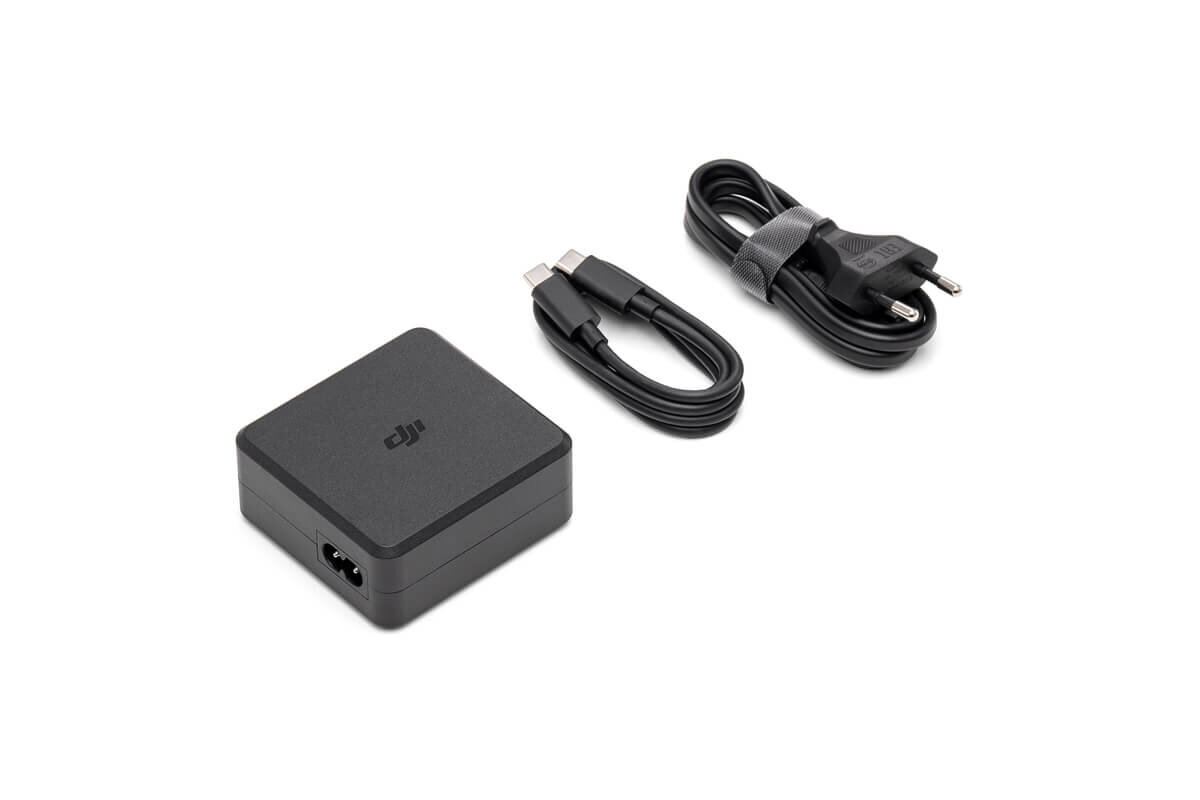 Na obrazie widoczna jest czarna ładowarka z logo \'dji\', kabel USB-C oraz kabel zasilający z wtyczką. Wszystkie elementy są ułożone na białym tle.