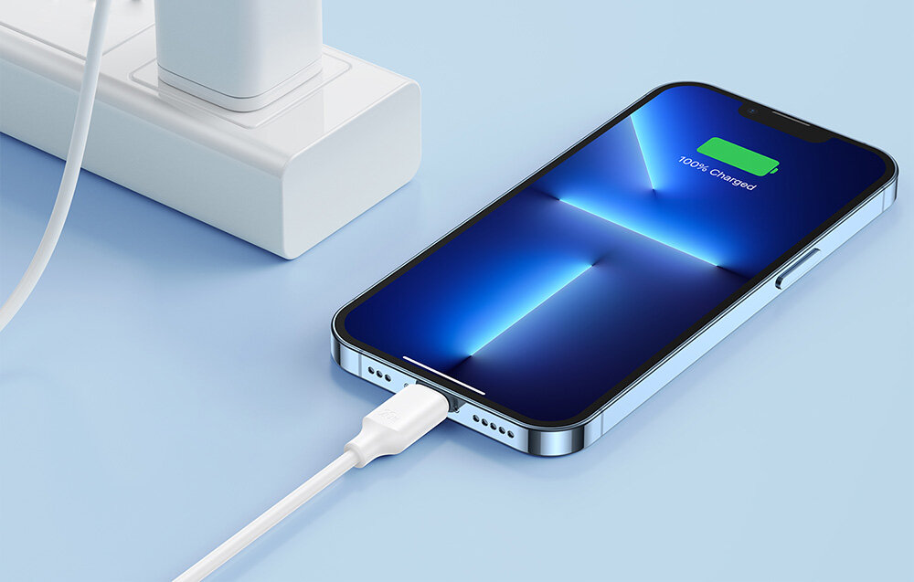 Smartfon z podłączonym kablem USB typu C jest ładowany, na ekranie widoczny jest wskaźnik naładowania z napisem \'100% Charged\'. Kabel jest podłączony do białej listwy zasilającej.