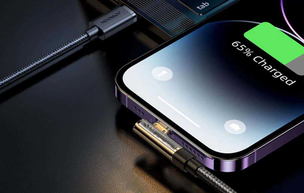 Na obrazie widać smartfon podłączony do kabla, z wyświetlaczem pokazującym \'65% Charged\'. Kabel ma metaliczną obudowę z widocznym logo \'JOYROOM\'.
