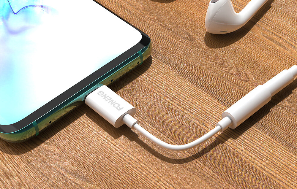 Na drewnianym blacie leży smartfon z podłączonym białym kablem audio, na którym widnieje napis \'FONENG\'. Kabel łączy się z białymi słuchawkami dousznymi.