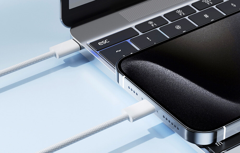 Na obrazie widać laptopa z klawiaturą, na której znajduje się klawisz \'esc\', oraz smartfon podłączony do laptopa za pomocą białego kabla USB-C. Kabel ma oplot i jest podłączony do obu urządzeń.