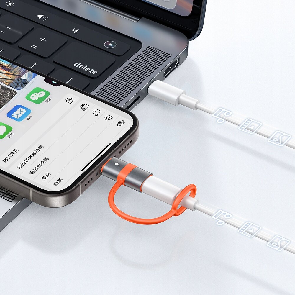 Zdjęcie przedstawia adapter USB-C do Lightning podłączony do iPhone\'a oraz laptopa, z widocznymi ikonami aplikacji na ekranie telefonu.