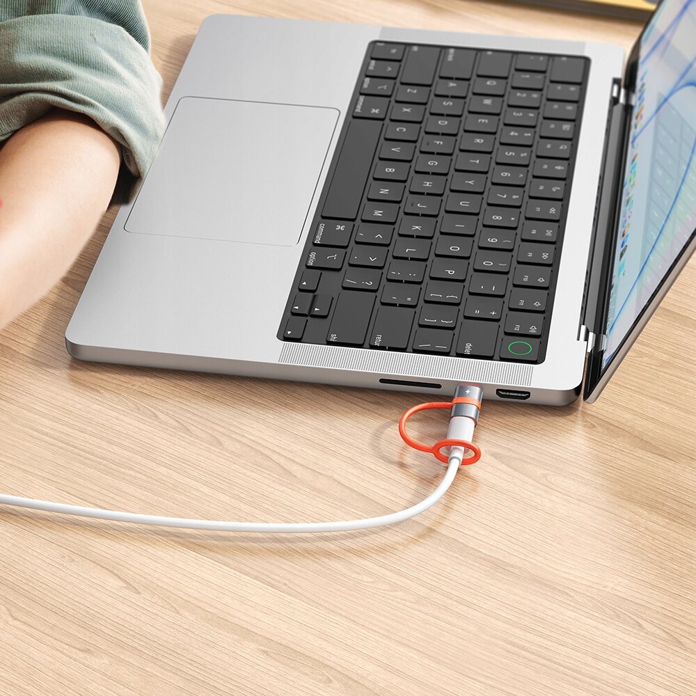Na drewnianym blacie znajduje się otwarty laptop z podłączonym kablem USB-C, który jest zabezpieczony czerwonym uchwytem.