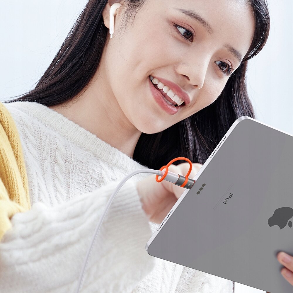 Osoba trzyma tablet z widocznym logo w kształcie jabłka, do którego podłączony jest kabel z pomarańczowym adapterem.