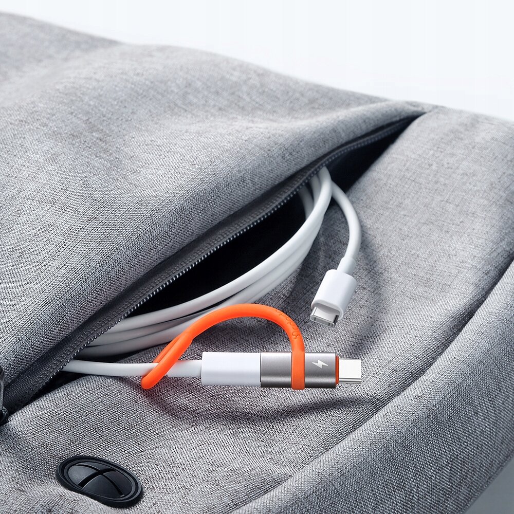 Zdjęcie przedstawia adapter USB-C do Lightning z pomarańczowym elementem, umieszczony na szarej tkaninie z zamkiem błyskawicznym.