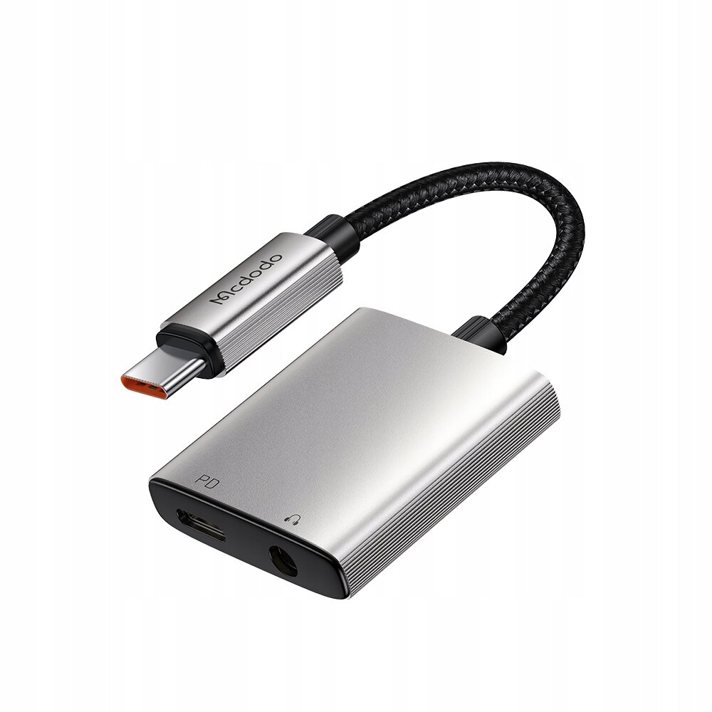Na obrazie widoczny jest srebrny adapter z logo \'Mcdodo\', posiadający złącze USB-C oraz porty PD i mini jack 3,5 mm. Kabel jest opleciony czarnym materiałem.