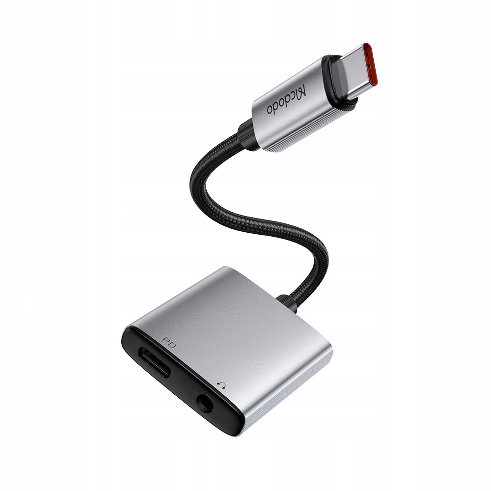 Na zdjęciu znajduje się srebrny adapter USB-C z napisem \'Mcdodo\' na wtyczce oraz dwoma portami oznaczonymi jako \'PD\' i symbolem słuchawek. Produkt jest przedstawiony na białym tle.