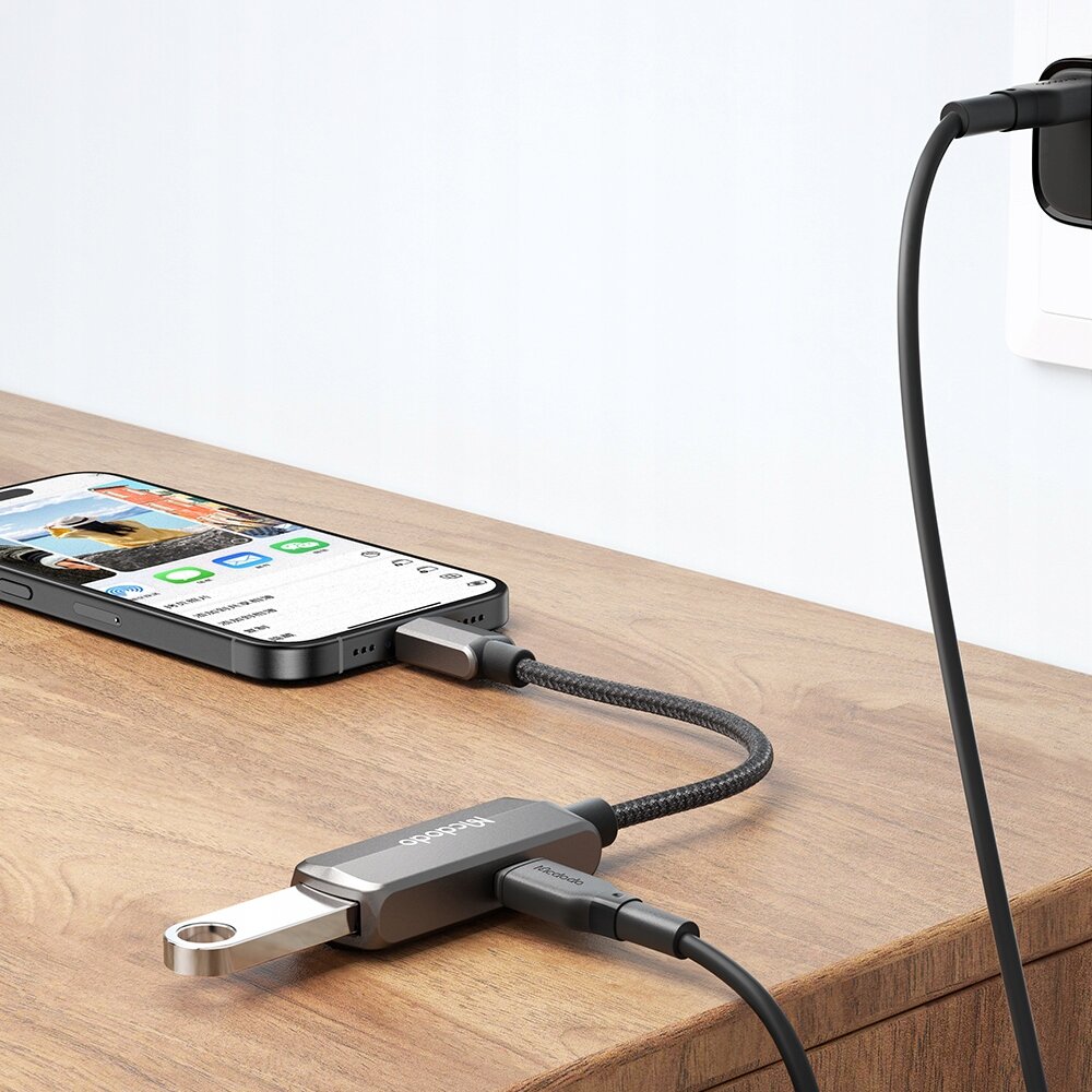Na zdjęciu znajduje się adapter USB-C na USB-A marki Mcdodo, podłączony do smartfona i pendrive\'a, leżący na drewnianej powierzchni. Na adapterze widoczne jest logo \'Mcdodo\'.