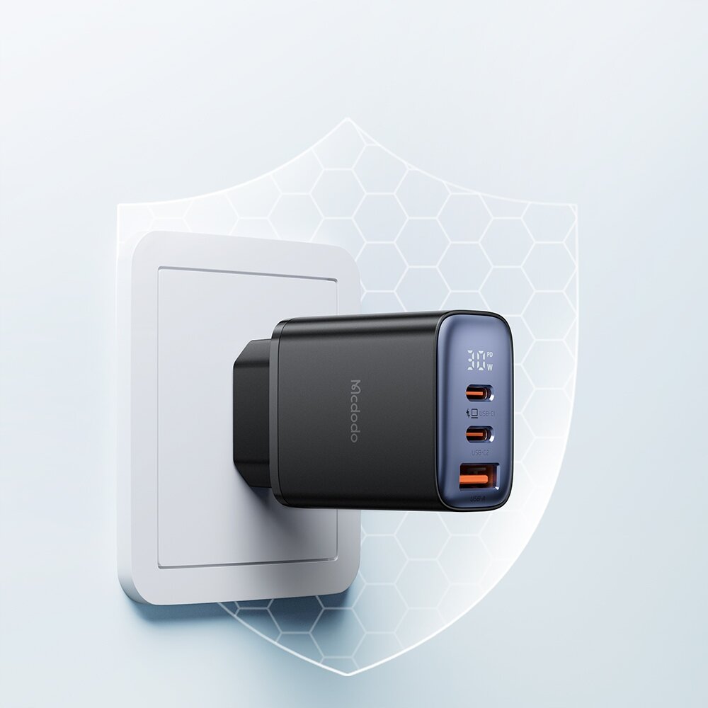 Na obrazie widoczna jest czarna ładowarka sieciowa z trzema portami: dwoma USB-C i jednym USB, podłączona do gniazdka. Na ładowarce znajduje się napis \'Mcdodo\' oraz oznaczenie \'30W\'.