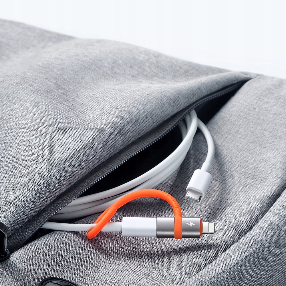 Zdjęcie przedstawia adapter USB-C do Lightning z pomarańczowym elementem, leżący na szarej tkaninie obok kabla USB-C. Adapter jest częściowo schowany w kieszeni materiałowej torby.