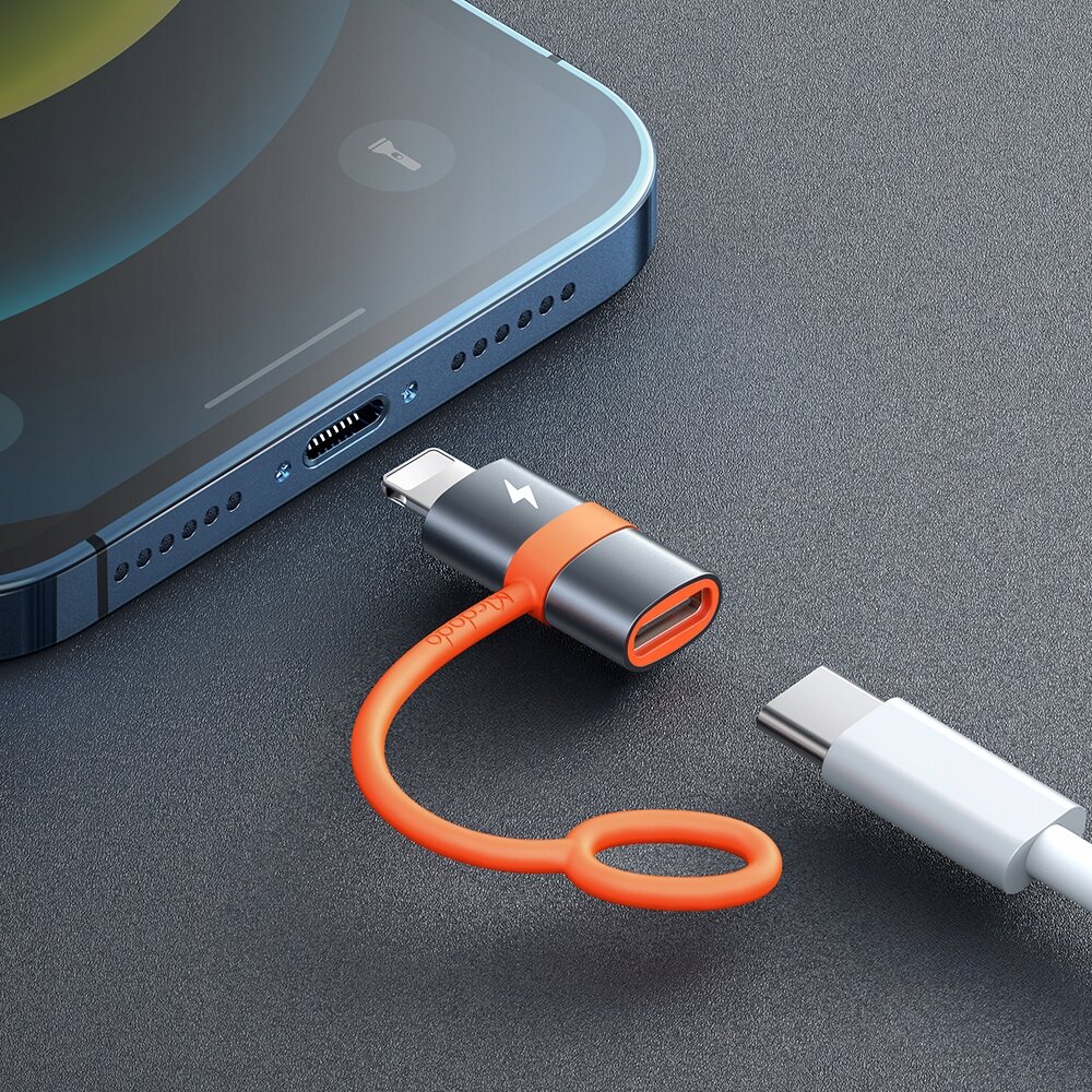Na obrazie widać adapter USB-C do Lightning z pomarańczowym kablem i szarym korpusem z symbolem błyskawicy. Obok znajduje się kabel USB-C oraz fragment smartfona z portem Lightning.