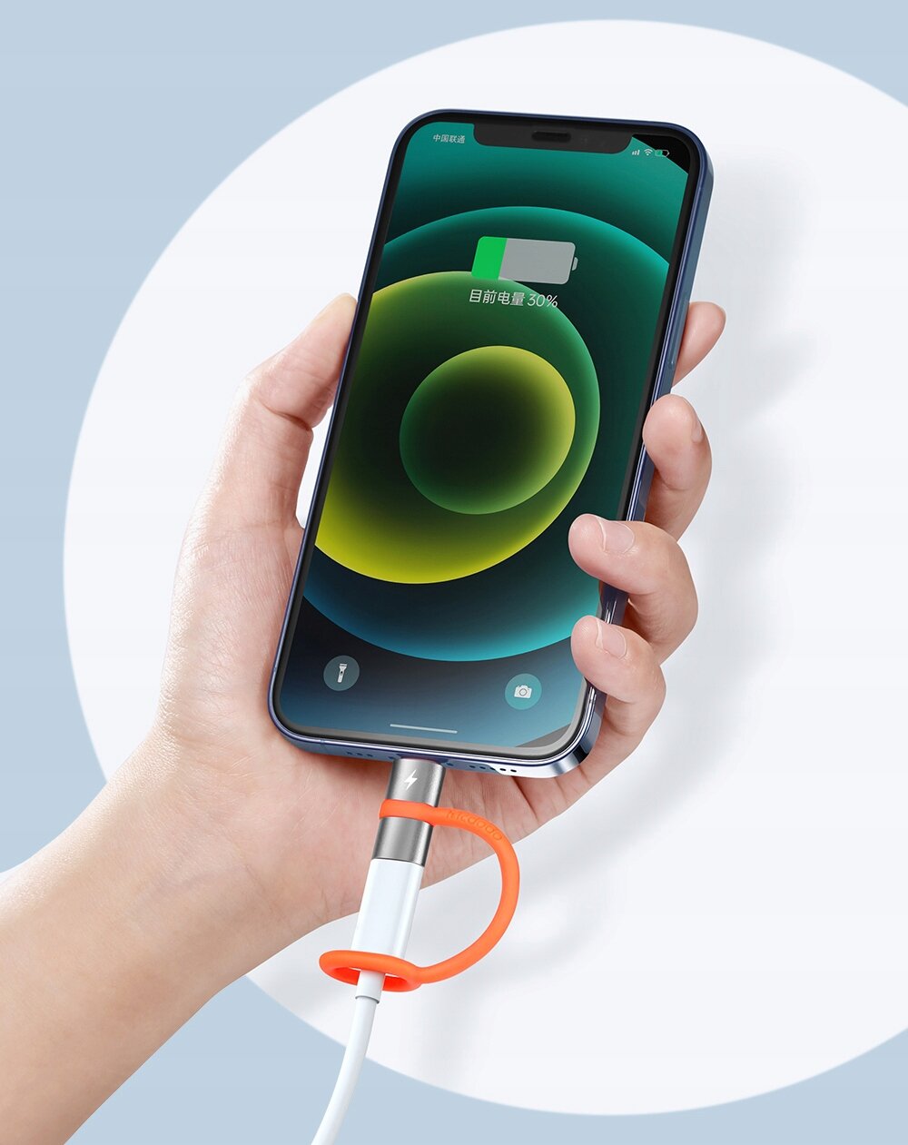 Osoba trzyma smartfon z podłączonym kablem przez adapter USB-C do Lightning. Na ekranie telefonu widoczny jest wskaźnik naładowania baterii z tekstem w języku chińskim oraz ikonami latarki i aparatu.