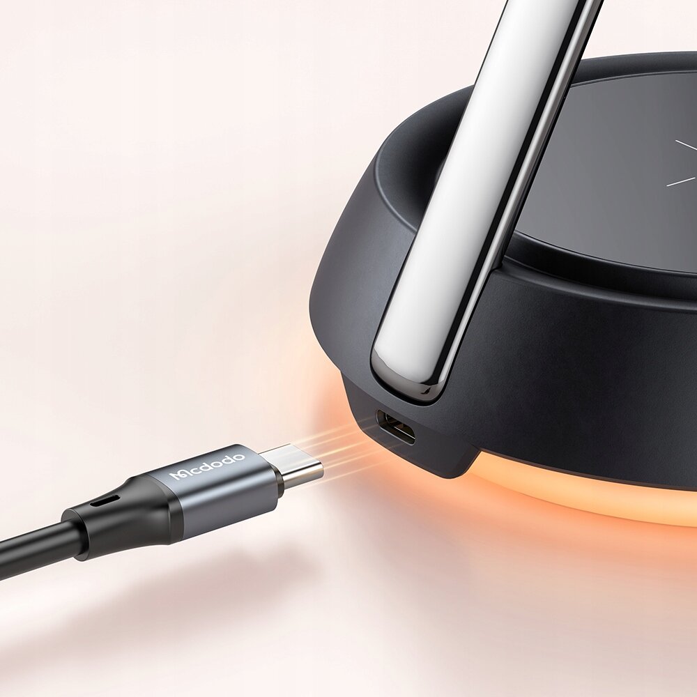 Obraz przedstawia czarną ładowarkę indukcyjną z metalowym uchwytem oraz podłączanym kablem USB-C z napisem \'Mcdodo\'.
