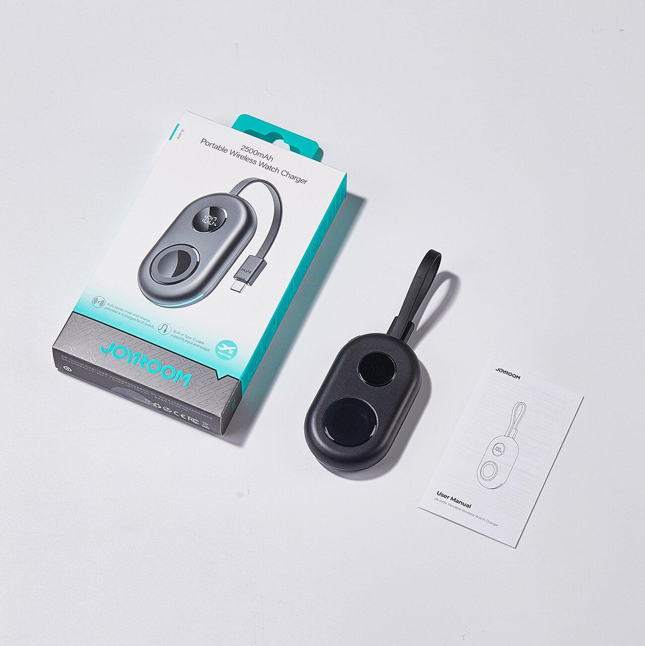 Na obrazie znajduje się czarna ładowarka bezprzewodowa z kablem oraz opakowanie z napisem \'JOYROOM\' i \'Portable Wireless Watch Charger\'. Obok leży instrukcja obsługi z rysunkiem ładowarki.