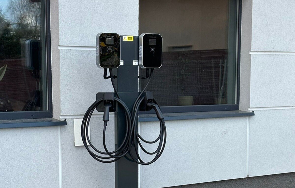 Ładowarka do samochodu elektrycznego BESEN BS20 App 22 kW Podwójna ładowarka do pojazdów elektrycznych z zawieszonymi kablami i wtyczkami przy oknie budynku.