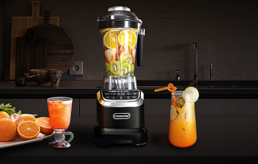 Na blacie kuchennym stoi czarny blender kielichowy z logo \'amzchef\', wypełniony owocami. Obok znajdują się dwa szklane naczynia z napojami oraz świeże pomarańcze.
