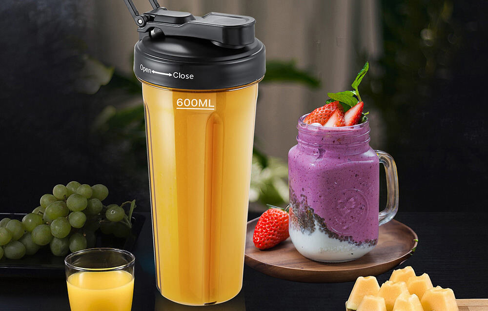 Na obrazie znajduje się blender kielichowy z napisem \'600ML\' oraz \'Open\' i \'Close\' na czarnym wieczku. Obok widoczny jest fioletowy smoothie w szklance z uchwytem, ozdobiony truskawkami i miętą.