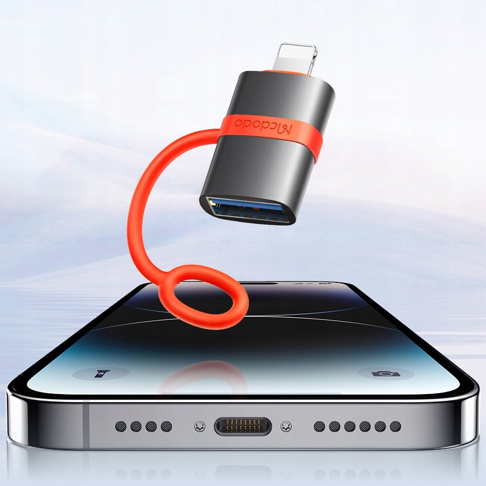 Na zdjęciu widoczny jest adapter USB-A 3.0 do Lightning z czerwonym kablem i napisem \'Mcdodo\' na tle smartfona. Tło jest jasne i neutralne, przypominające niebo lub wodę.