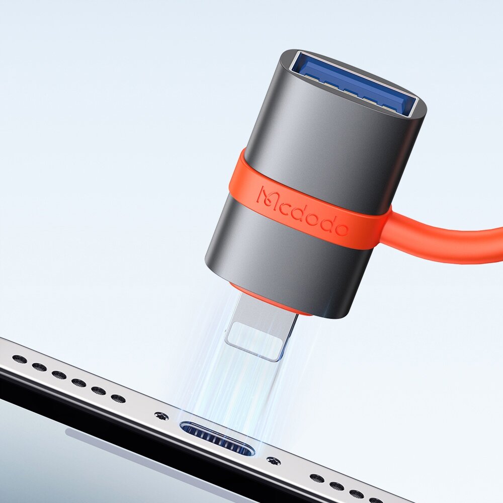 Na obrazie widoczny jest adapter USB-A 3.0 do Lightning z logo \'Mcdodo\' na obudowie. Adapter jest podłączany do urządzenia z portem Lightning.