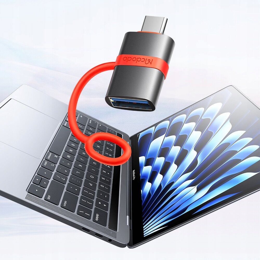 Na zdjęciu widoczny jest adapter Mcdodo z czerwonym kablem, podłączony do laptopa z otwartym ekranem. Na adapterze znajduje się napis \'Mcdodo\'.