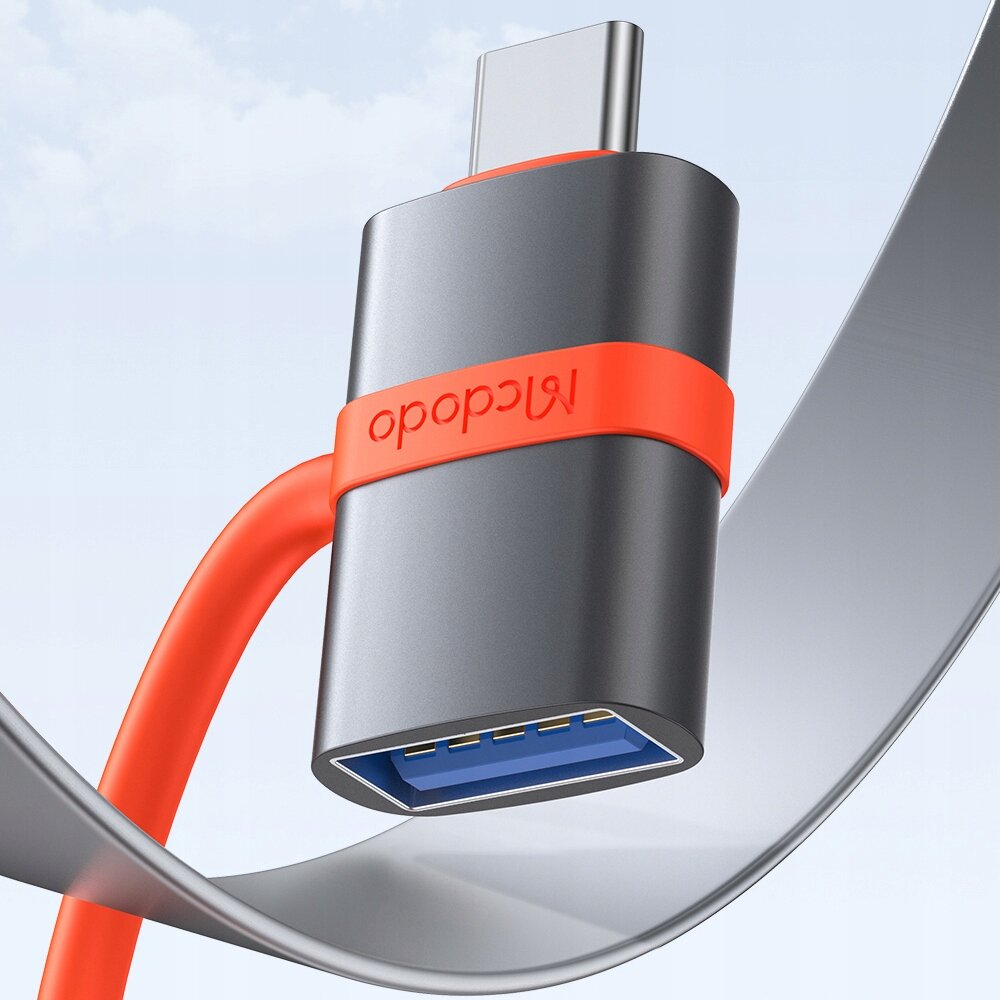 Na obrazie widoczny jest adapter USB z szarym korpusem i czerwonym elementem z napisem \'Mcdodo\'. Adapter ma złącze USB-C i port USB-A z niebieskim wnętrzem.