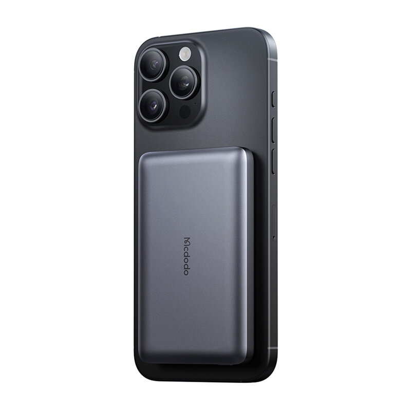 Na obrazie widoczny jest smartfon z przymocowanym magnetycznym powerbankiem w kolorze ciemnoszarym. Na powerbanku znajduje się napis \'Mcdodo\'.