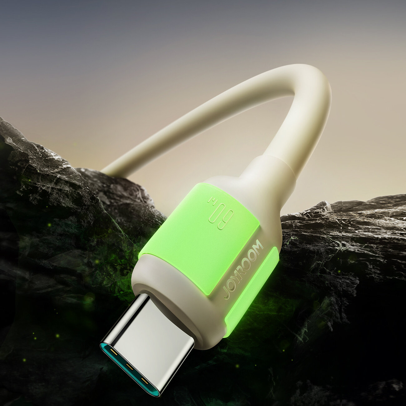 Obraz przedstawia kabel USB-C z jasnozieloną osłoną, na której widnieje napis \'JOOM\'. Kabel leży na ciemnym, skalistym tle.