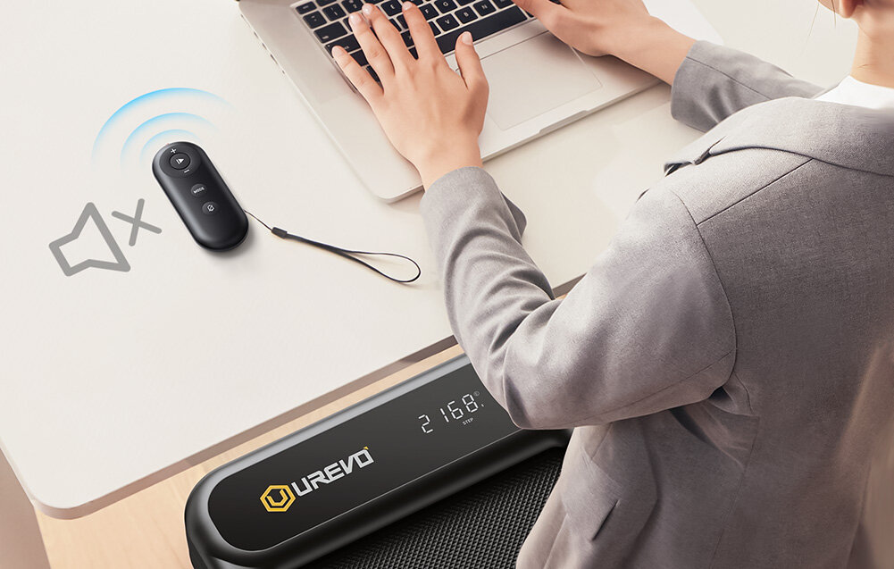 Bieżnia elektryczna UREVO Strol 2E Smart 2w1 550W 10km-h pokój biurko osoba korzysta z bieżni na biurku leży pilot złożysz do wymiarów 57.3 x 11.7 x 130 cm Silnik o mocy 2,5 HP stabilną, cichą pracę wbudowany pilot z funkcją wyciszenia Pilot zasilany jest baterią pastylkową CR2032 3V