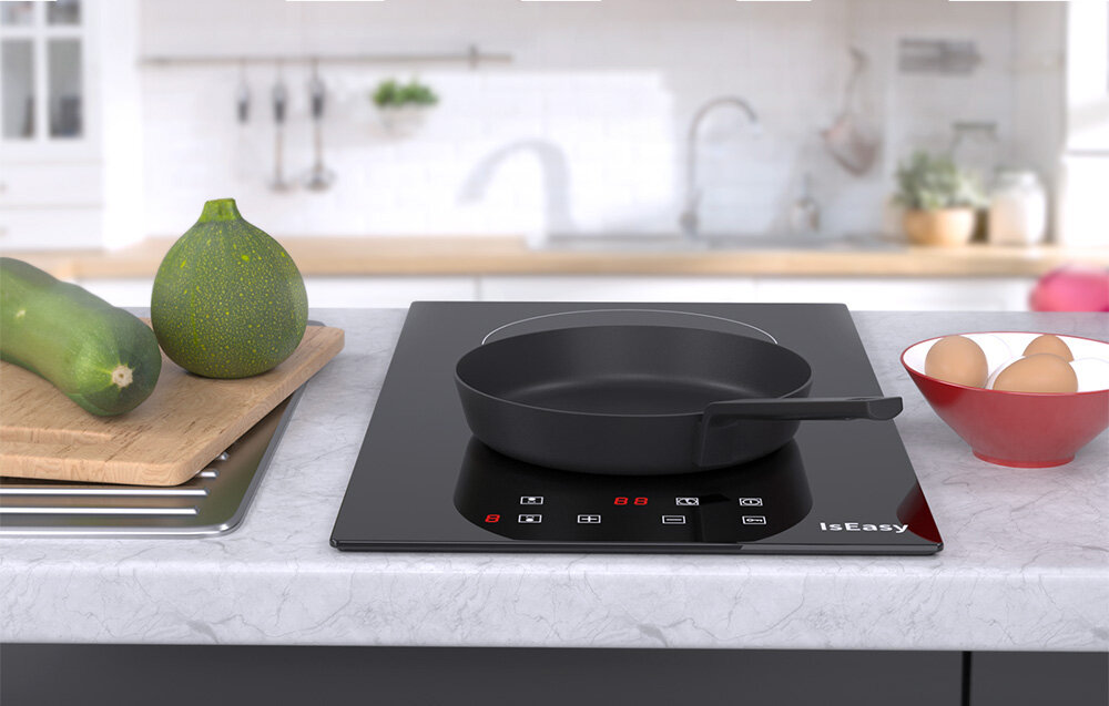Płyta ceramiczna ISEASY T2V-01M Na płycie grzewczej stoi czarna patelnia, a obok znajdują się warzywa i miska z jajkami. Scena kuchni jest jasna i uporządkowana płyta do małej kuchni kompaktowa zabudowa