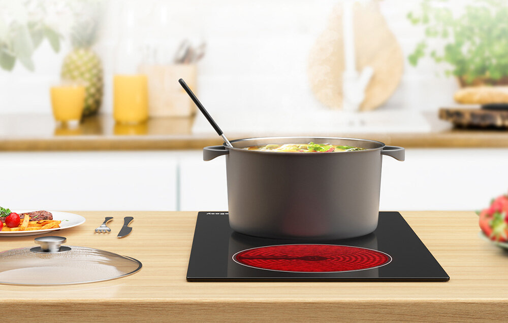 Płyta ceramiczna ISEASY LT2V-30 Duży czarny garnek stoi na rozgrzanej strefie płyty promiennikowej, a z jego wnętrza unosi się para. Obok leży szklana pokrywka i świeże składniki różne naczynia stal żeliwo ceramika