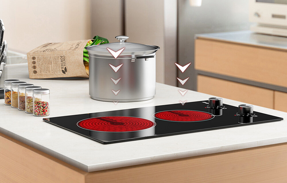 Płyta ceramiczna ISEASY LT2V-30 Strzałki skierowane w dół podkreślają równomierne przekazywanie ciepła z płyty na stojący na niej garnek. Wokół znajdują się przyprawy i torba z warzywami płyta wolnostojąca montaż w blacie