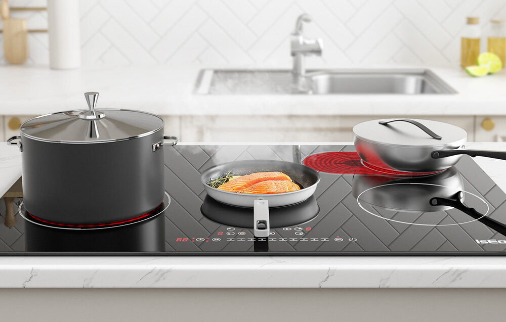 Płyta ceramiczna ISEASY LT5-04 Na płycie stoją trzy naczynia: duży garnek, patelnia z rybą oraz mały rondelek, a każde z nich znajduje się na aktywnym polu grzewczym. Z garnków unosi się delikatna para