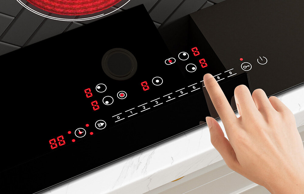 Płyta ceramiczna ISEASY LT5-04 9 poziomów mocy blokada dzieci Zbliżenie na panel sterowania pokazuje czerwone cyfry i ikonki, a palec wybiera jedno z ustawień mocy. Układ przycisków jest równy i czytelny