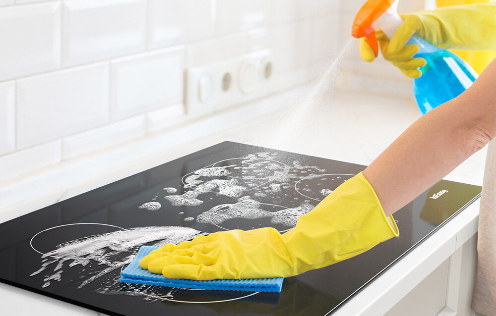 Płyta ceramiczna ISEASY LT5-04 Ręka w żółtej rękawicy czyści płytę grzewczą spryskaną detergentem, tworząc pianę na powierzchni. Ujęcie podkreśla łatwość czyszczenia gładkiej tafli szklana powierzchnia łatwe czyszczenie