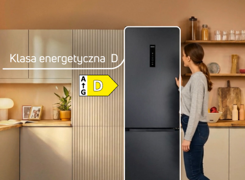 Kobieta stoi obok czarnej lodówki w kuchni, na której widoczna jest etykieta z klasą energetyczną D. W tle znajdują się szafki kuchenne i półki z naczyniami.