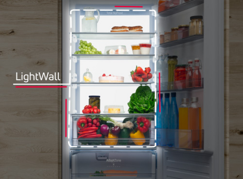Otwarta lodówka z widocznymi półkami wypełnionymi różnorodnymi produktami spożywczymi, takimi jak owoce, warzywa i napoje. Na drzwiach lodówki widoczny jest napis \'LightWall\'.